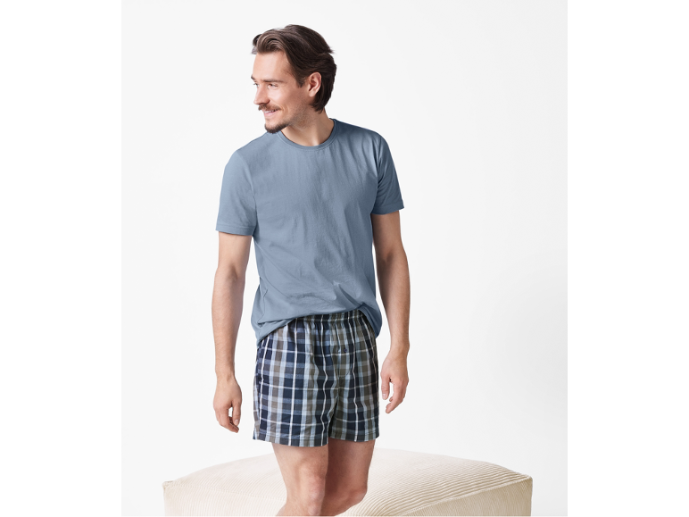 Man in blue t-shirt and plaid boxers, standing on an ottoman.
