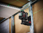Laser level mounted on a metal frame, projecting green laser lines onto walls and ceiling.