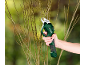 A hand holds electric pruning shears cutting tree branches against a blurred background.