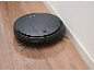Black robotic vacuum cleaner on a wooden floor, cleaning along a wall.