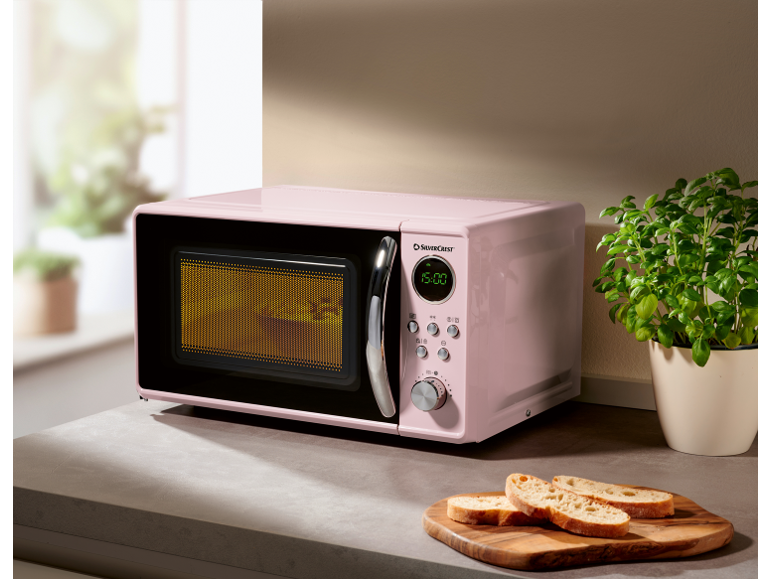 Pink microwave on a kitchen counter with herbs and bread slices.