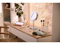 Dressing table with an illuminated mirror, cosmetics, and brushes, by a window with blinds.