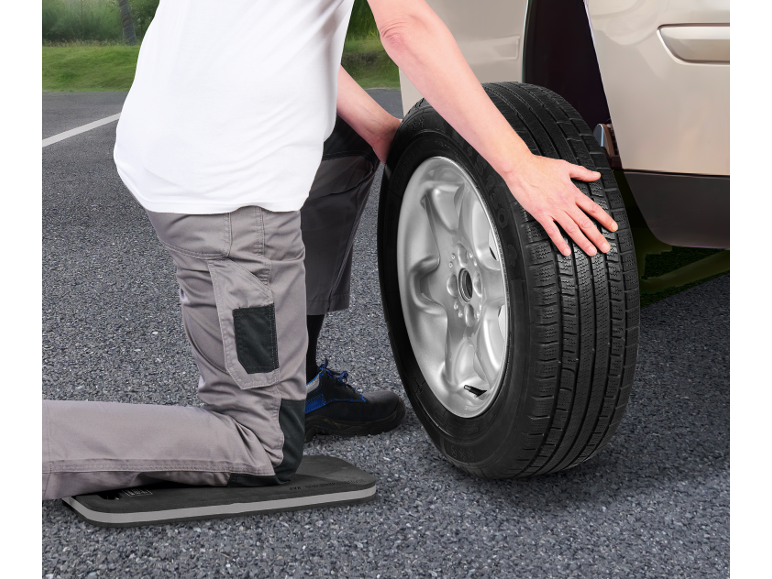 Man kneeling changing a car tire, using a kneeling pad.