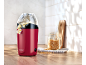 Red popcorn maker with popcorn on a wooden countertop, next to a jar of corn kernels.