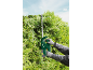Green electric hedge trimmer cutting a cypress hedge under a blue sky.