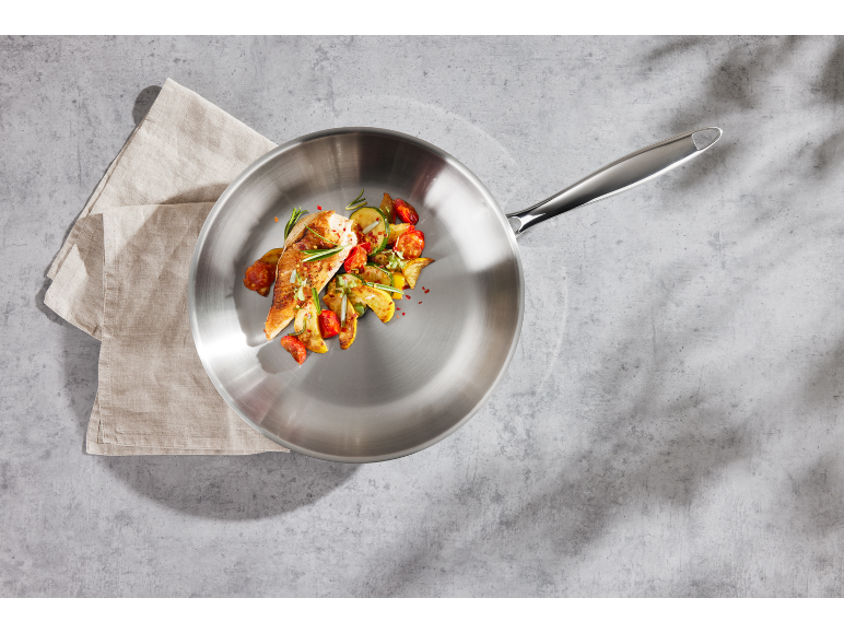 Frying pan with chicken and vegetables on a concrete background with a kitchen towel.