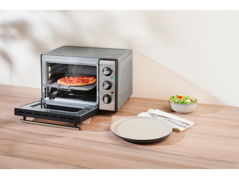 Mini oven with pizza, ready to be served with a side salad and plate.