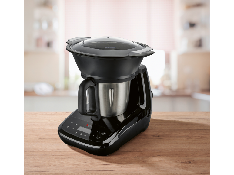 Black kitchen machine with stainless steel bowl and transparent lid on a wooden table.