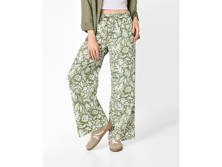 Women's wide-leg trousers with green and white floral print, paired with a green shirt and beige sneakers.