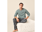 Man in green long-sleeve top with 'Slowdown' text and plaid pajama pants, sitting on an ottoman.