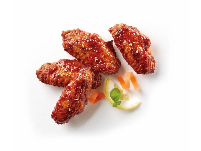 Four glazed chicken wings with lemon and carrot garnish on a white background.