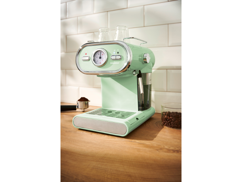 Mint-colored retro coffee machine with cups and coffee beans on a wooden counter.