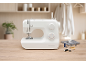 White sewing machine on a wooden table with threads and sewing accessories.