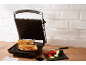 Sandwich maker with two grilled sandwiches and fresh vegetables in a kitchen.