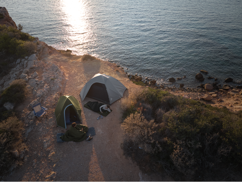 Two tents and two people camping by the sea at sunset.