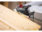 Electric planer smoothing a wooden board, hands wearing gloves.