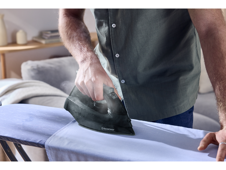 A person ironing a light blue shirt on an ironing board with a dark iron.