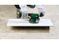 Hands using a cordless power tool on a white board on a concrete floor.