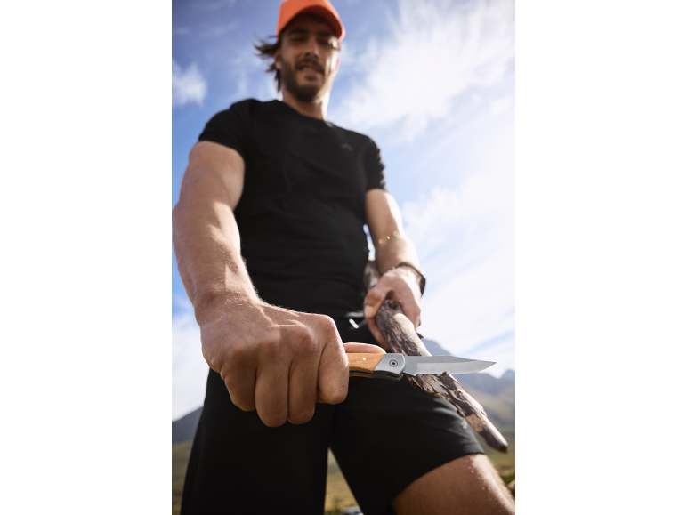 Man in a cap and t-shirt holding a folding knife and a stick.