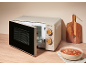 Beige microwave with open door, bowl of soup, and wooden cutting board on a countertop.