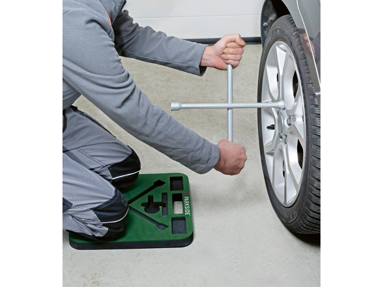Man changing a car wheel using a cross wrench and a kneeling pad.