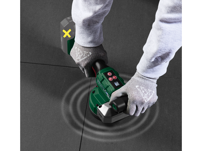 Man with gloved hands uses a tile vibrator on dark tiles.