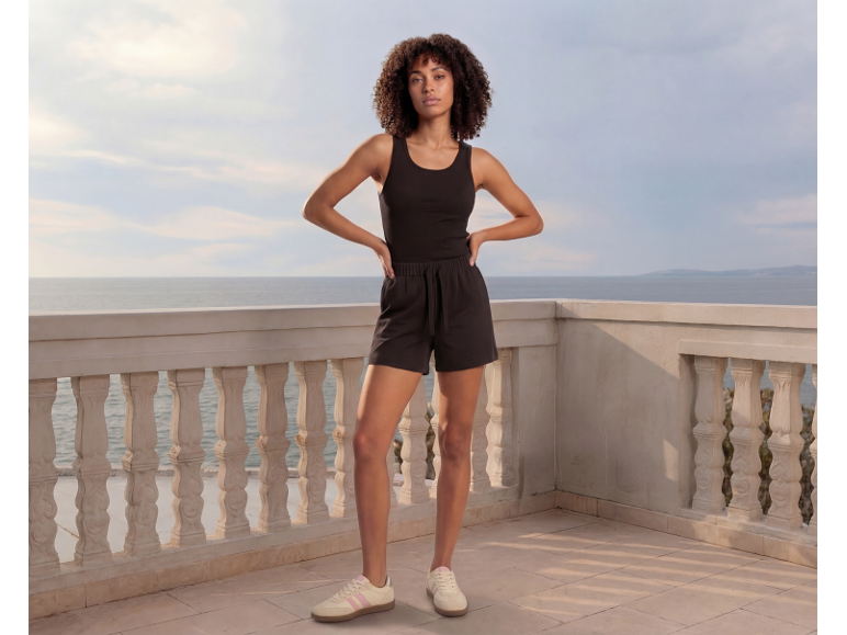 Woman in black tank top and black shorts on a balcony overlooking the sea.