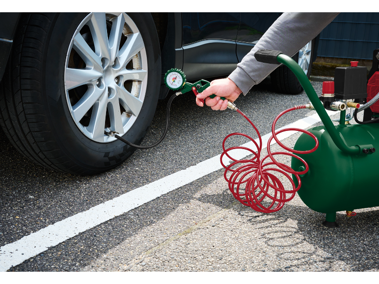 Person inflating a car tire with a portable air compressor and pressure gauge.