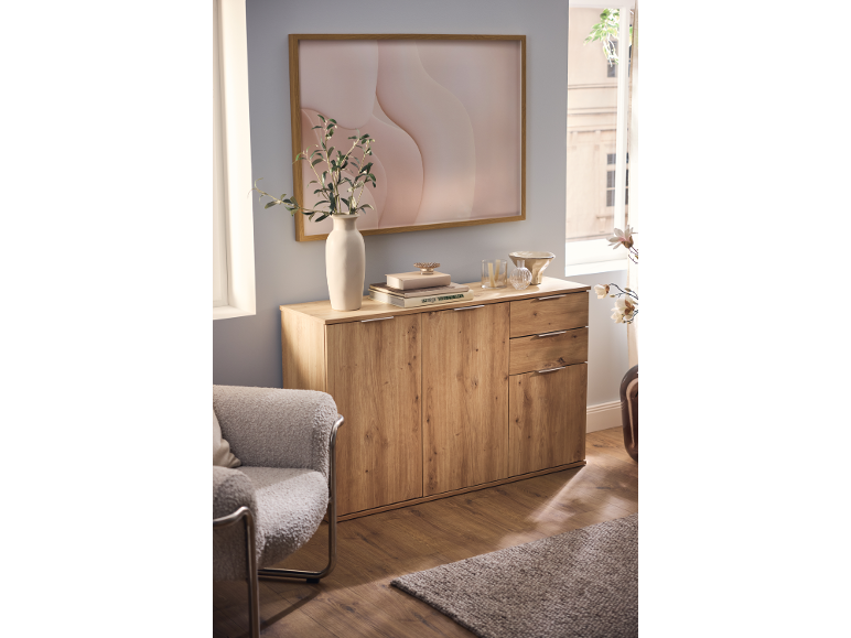 Wooden sideboard with decor, a vase with branches, and a framed abstract art print.
