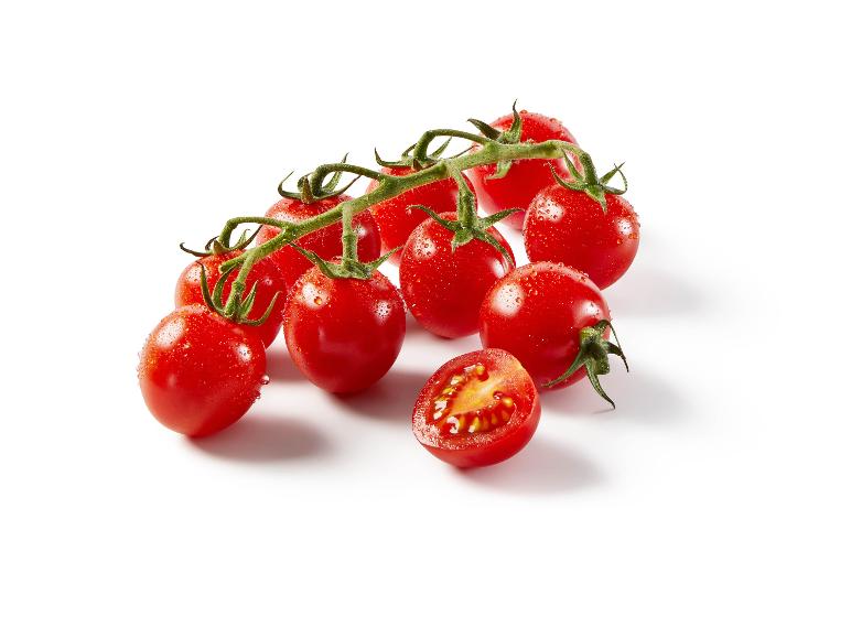 Red cherry tomatoes on the vine with water droplets, one tomato cut in half