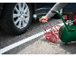 Person inflating a car tire with a portable air compressor and pressure gauge.