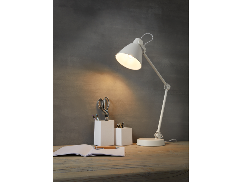 White desk lamp illuminates a desk with a notebook, pens, and scissors.