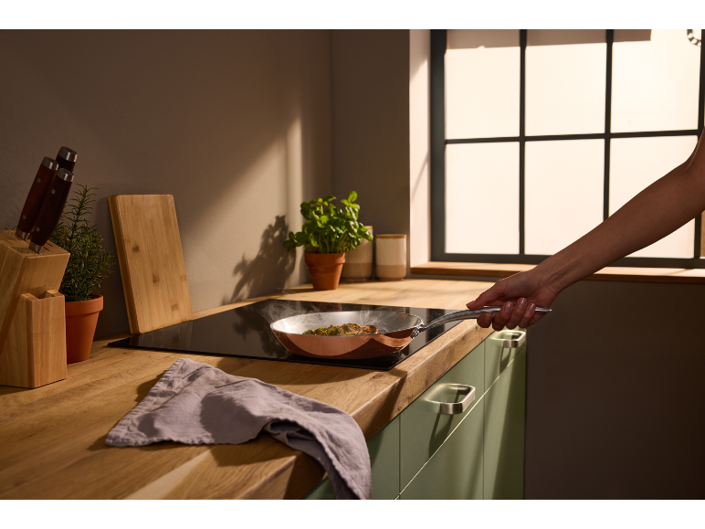 Modern kitchen with a copper pan on a hob, held by a hand.