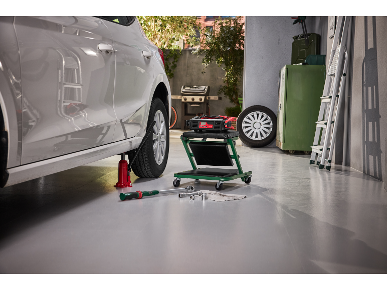 Car on a jack in a garage with tools and a battery charger.
