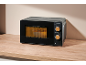 Black microwave with wooden details on a wooden countertop, with food inside.