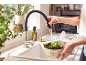 Kitchen faucet with flexible hose rinsing lettuce in a colander over the sink.