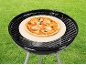 Pizza on a pizza stone on an outdoor charcoal grill