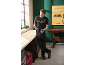 Man in black t-shirt and work trousers holding a cordless drill and battery in a workshop.