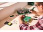 Man soldering a circuit board with a soldering iron, solder wire, and other tools on a workbench.