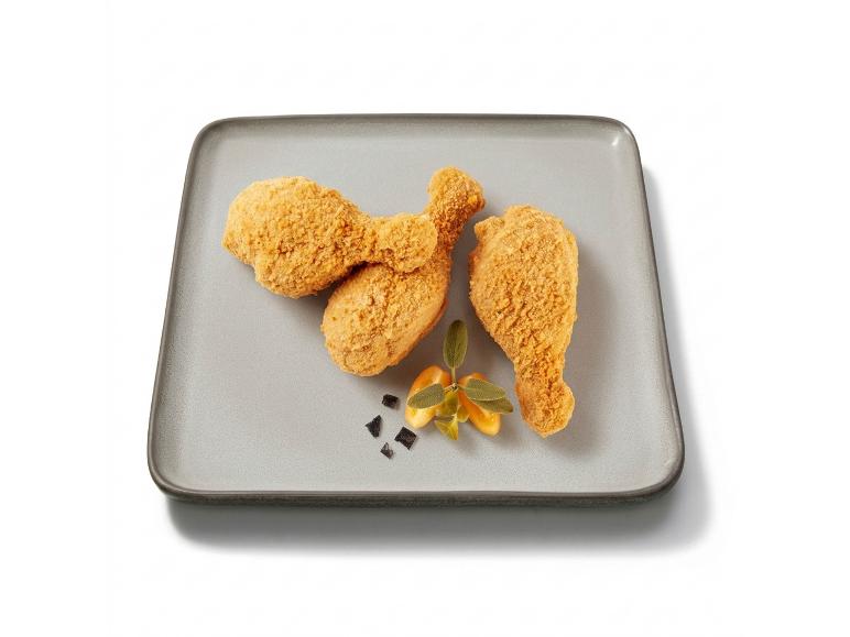Three breaded chicken drumsticks on a gray rectangular tray, decorated with herbs.