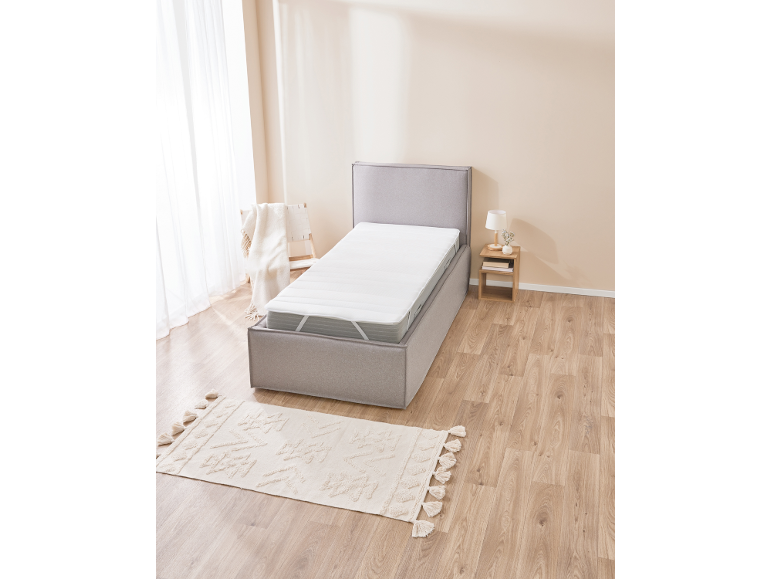 Single bed with grey upholstered frame, white mattress, and a cream rug on a wooden floor.