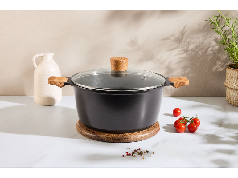 Black pot with wooden handles and glass lid on a wooden trivet.