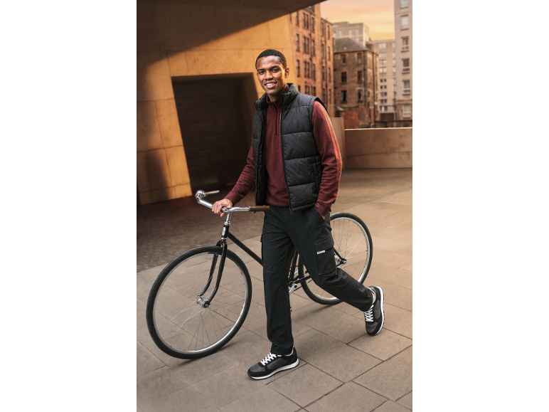 Man in black puffer vest, maroon sweatshirt, and cargo pants with a bicycle.