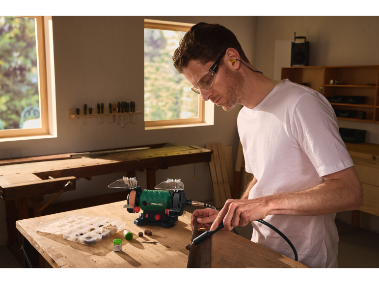 Man using a bench grinder and rotary tool in a workshop.