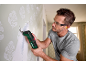 Man using a multi-tool to remove wallpaper, wearing safety glasses and earplugs.