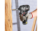 Gloved worker using a cordless impact driver to screw a screw into wood.