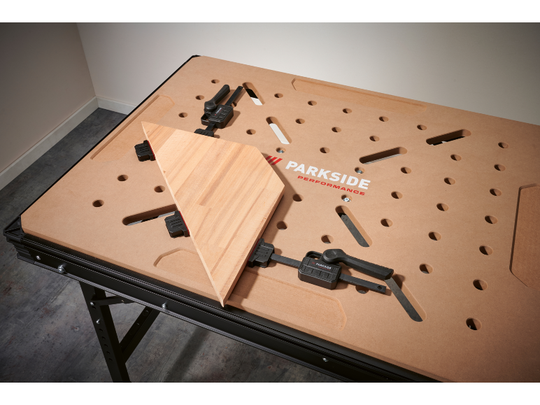 Workbench with a wooden board secured by clamps.