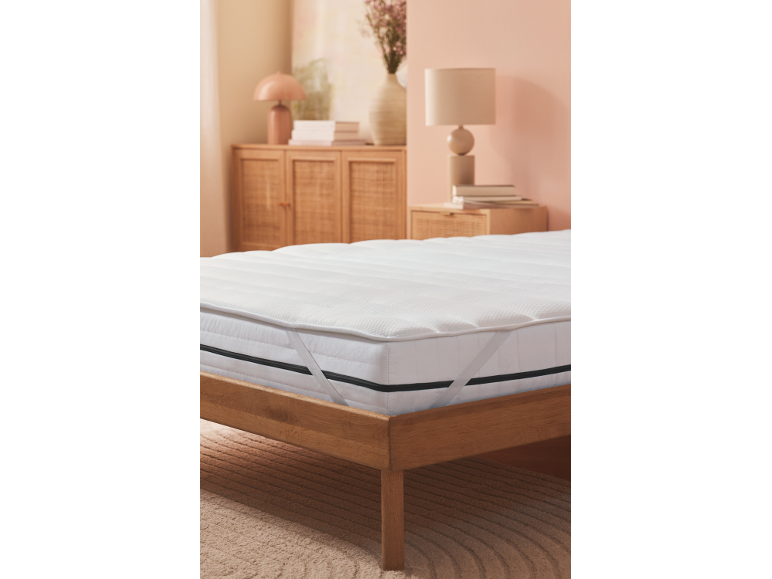 White mattress topper on a wooden bed in a soft-toned bedroom.