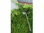 Long-reach hedge trimmer cutting a green hedge in front of a house.