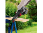 Gloved person using a cordless mini chainsaw to cut a wooden board outdoors.